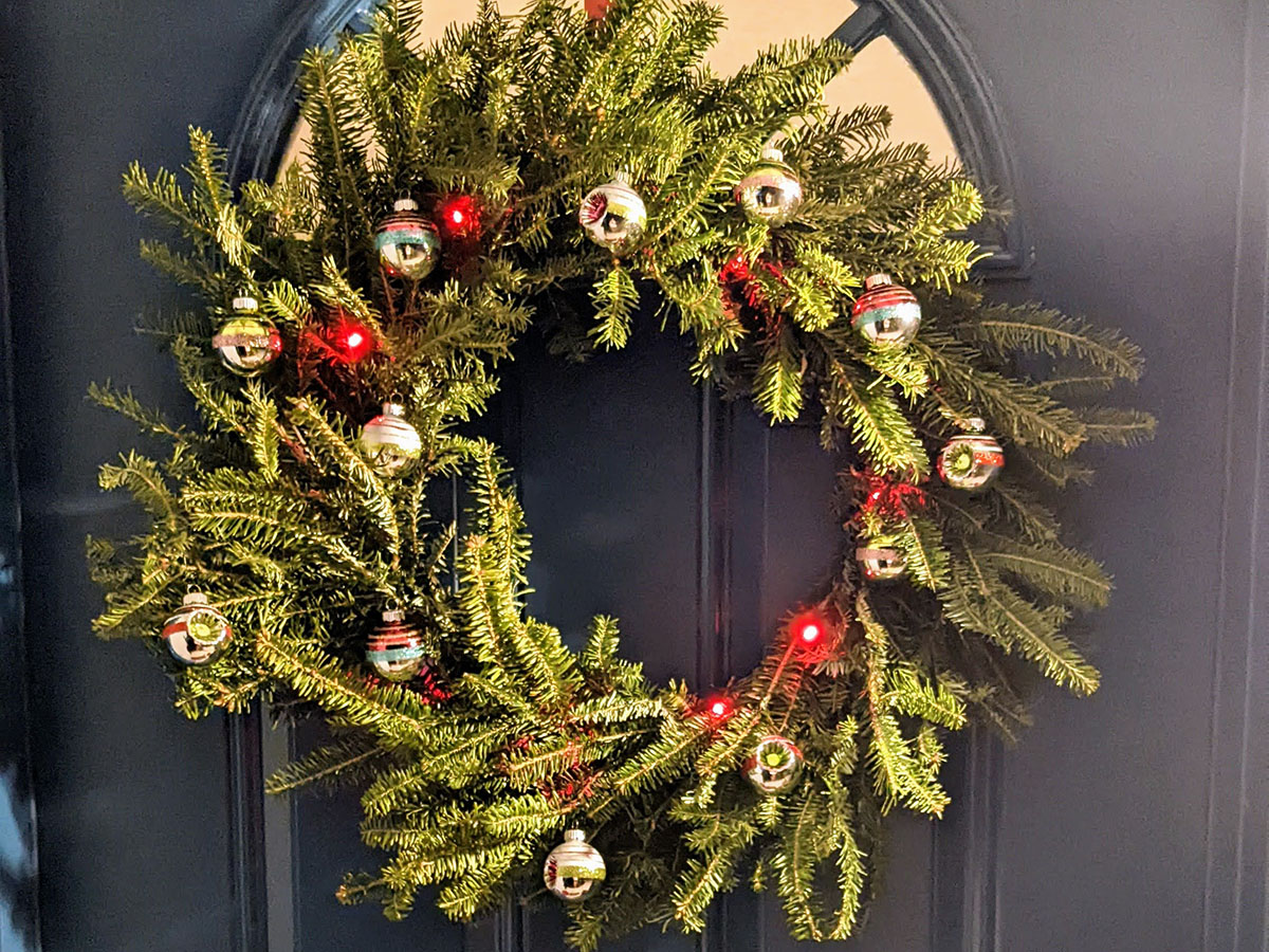 How to make a wreath for beginners: lush green wreath with red lights and red and silver ornaments on blue door